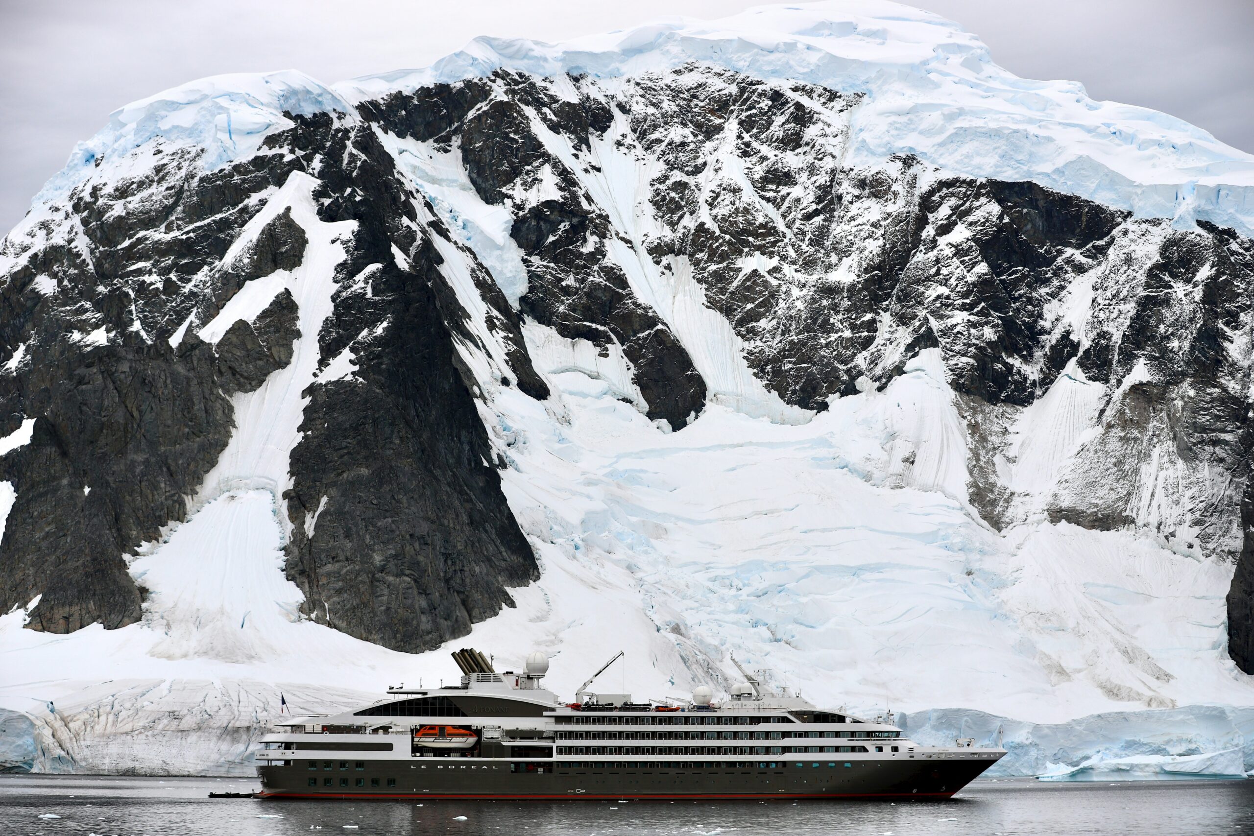 A cruise ship sails in the icy Antarctic waters with a snowy mountain in the background.