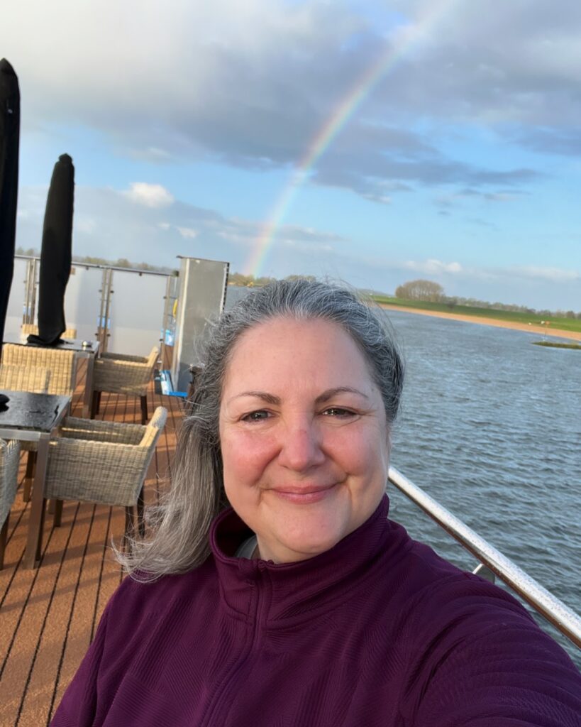 Michele on the AmaMora sundeck with a rainbow in the background, enjoying the peaceful experience of river cruising.